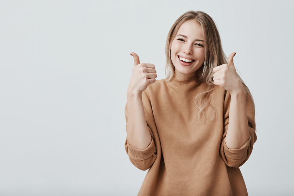 Young woman holding two thumbs up while smiling.