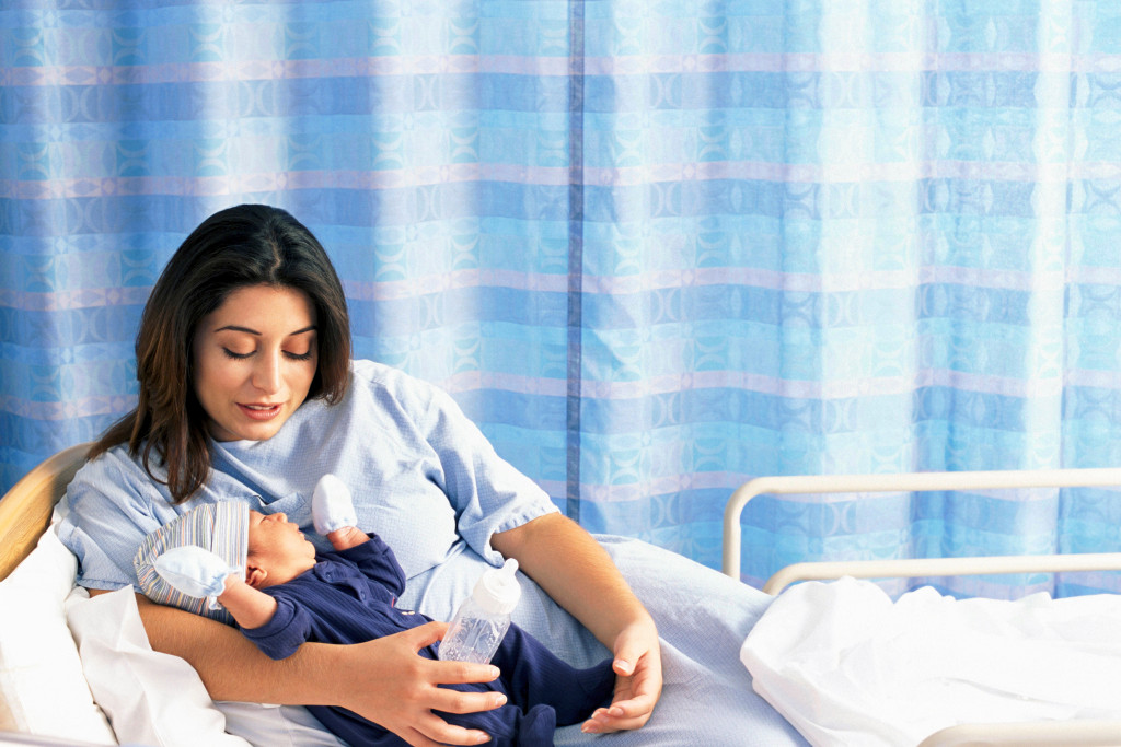 A mother holding her baby with complete care while lying on a hospital bed